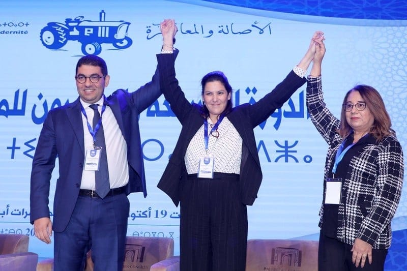 Three PAM leaders on stage with raised arms at a National Council session